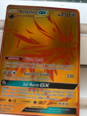 Solgaleo GX Pokémonkort guld - Unikt Solgaleo GX Pokémonkort i guldutförande med holografisk effekt. Kortet har en cool design med Solgaleo i orange och guld, och detaljerad text om attacker och förmågor. Perfekt för samlare eller Pokémonfans som vill utöka sin kortsamling.