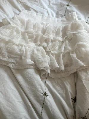 Vita volangtrosor med rosett - Söta vita trosor med flera lager volanger och en liten satinrosett framtill. Tillverkade i ett tunt, luftigt tyg som ger en romantisk och lekfull känsla. Perfekta för dig som gillar gulliga detaljer och mjuka material.