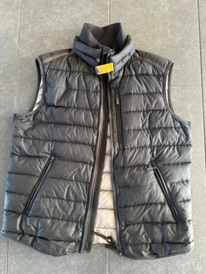 Svart dunväst från Parajumpers - Snygg svart dunväst från parajumpers. Västen har två dragkedjeförsedda fickor fram och en bröstficka. Quiltad design och diskret logga bak i nacken. Perfekt för lager på lager och streetwear.