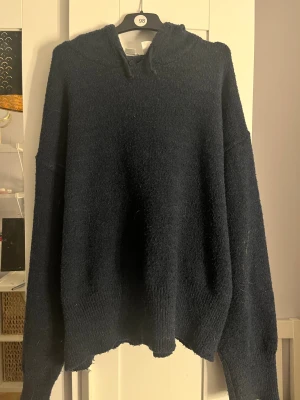 Mörkblå fluffig hoodie - Mysig mörkblå hoodie med fluffig och stickad känsla. Tröjan har huva och långa ärmar, perfekt för att chilla i. Materialet ser ut att vara mjukt och lite luddigt, vilket ger en avslappnad vibe. Passar dig som gillar oversized och bekvämt.