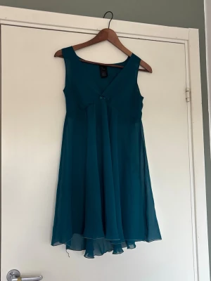 Blå ärmlös kortklänning med v-ringning - Säljer en blå ärmlös kortklänning med v-ringning och lätt volang i nederkanten. I mesh material