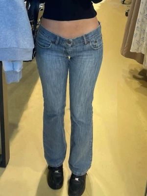 Blå bootcut jeans från No more, LOW WAIST! - Snygga blå bootcut jeans från No more med klassisk femficksdesign och diskreta slitningar. Jeansen har låg midja och raka ben med lätt utsvängning. Perfekta för en avslappnad och trendig look.