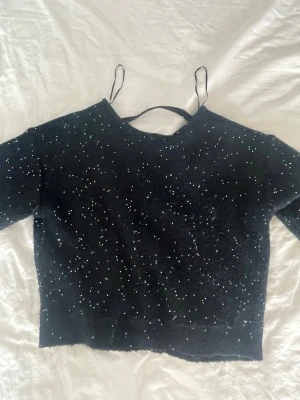 Svart glittrig croppad sweatshirt - Snygg svart croppad topp med glittriga detaljer över hela tyget. Toppen har en rund halsringning och är kort i modellen, perfekt för att sticka ut. Materialet känns mjukt och stretchigt, och tröjan har långa ärmar.