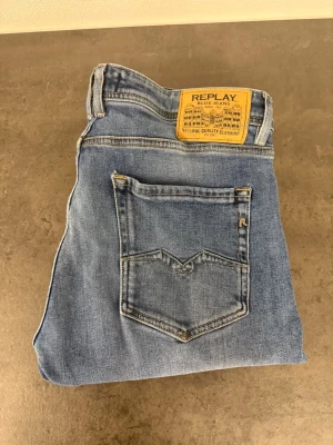 Ljusblå raka jeans från Replay 34/32 - Säljer ett par ljusblå jeans från Replay med klassisk femficksmodell och raka ben. Jeansen har en snygg tvätt och detaljerad bakficka med Replay-logga samt patch i läderimitation bak i midjan. Perfekta till en avslappnad stil.