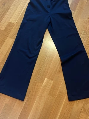 Mörkblå kostymbyxor från Weekday - Snygga mörkblå kostymbyxor från Weekday med raka, vida ben och klassisk midja. Byxorna har diskreta fickor fram och stängs med knapp och dragkedja. Perfekta för en clean och stilren look.