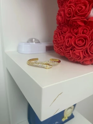 Guldigt armband med pärldetaljer - Snyggt armband i guldfärg med öppen design och vågig form. Armbandet är dekorerat med små vita pärlor längs ovansidan som ger en lyxig och trendig känsla.