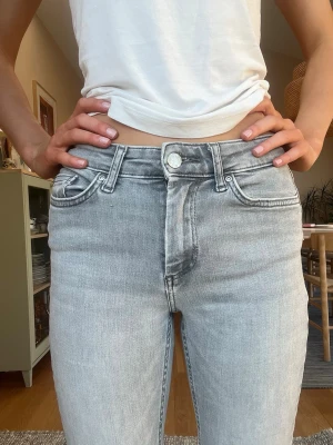 Ljusgrå bootcut jeans med medel midja - Säljer ett par ljusgrå jeans med bootcut ben och medel midja. Jeansen har klassisk femficksdesign, bälteshällor och silverfärgad knapp. Materialet är denim i bomull med en lätt tvättad look. Perfekta för en avslappnad och trendig stil.  Storlek XS/32 i midja och 30 i längd. 