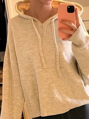 Beige hoodie med huva och dragsko - Mysig beige hoodie med huva och dragsko, tillverkad i ett mjukt stickat material. Hoodien har ribbade muddar vid ärmslut och nederkant samt en avslappnad passform. Perfekt för en chill och avslappnad stil.