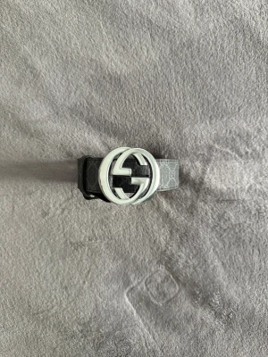 Gucci bälte  - Säljer ett svart skinnbälte från Gucci med klassiskt GG-mönster och en stor silverfärgad GG-spänne. Bältet har en stilren och lyxig design som lyfter vilken outfit som helst. Perfekt för dig som vill ha något exklusivt och trendigt.