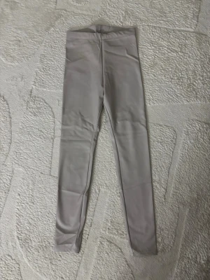 Beige höga leggings i fuskskinn - Snygga beige leggings i fuskskinn-look med hög midja och smal passform. Stretchigt material som sitter tajt och bekvämt. Inga synliga fickor eller dragkedjor.