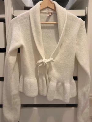 Vit stickad kofta - Supersöt vit stickad kofta med volangkant nedtill och knytning från Nelly.