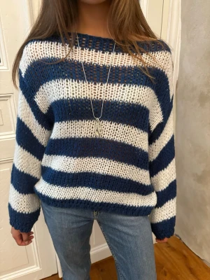 Randig blåvit stickad tröja - Säljer en stickad tröja med breda blå och vita ränder. Tröjan har en lös passform, långa ärmar och rund halsringning. Materialet ser ut att vara mjukt och lite fluffigt, perfekt för kyligare dagar. Passar dig som gillar en avslappnad och trendig stil.