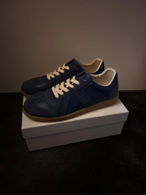 Maison Margiela Gats - Snygga marinblå sneakers med beige gummisula och vita skosnören. Ovandelen är i läder och mocka med klassisk retrostil. Insidan är ljus och skon har en låg profil som passar till många olika outfits.