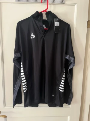 Select Training sweat 1/2 zip Spain, träningströja - Svart strl L - Svart långärmad träningströja från Select modell Spain med halv dragkedja och ståkrage. Material: 100% polyester. Nyskick aldrig använd med etikett. Storlek L.