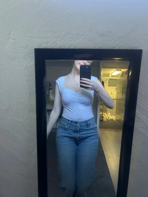 Vit croppad topp med rynkdetalj - Säljer en vit body med rynkdetalj framtill och breda axelband. Toppens passform är tight och den har en snygg v-ringning. Perfekt att matcha med jeans eller kjol för en trendig look. Strl M men passar S 🤍