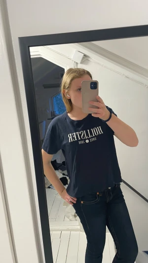 Mörkblå Hollister t-shirt med tryck - Säljer en mörkblå t-shirt från Hollister med vitt tryck på bröstet. T-shirten har korta ärmar och en klassisk rund halsringning. Perfekt för dig som gillar en enkel och stilren look med en touch av amerikansk streetstyle.