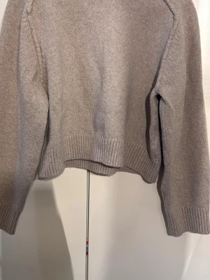 Beige stickad tröja från H&M - Mysig beige stickad tröja från H&M med ribbstickade muddar och nederkant. Tröjan har en klassisk rak passform och är tillverkad i mjukt material som passar perfekt för kyliga dagar.