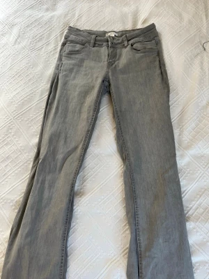 Grå bootcut jeans med dubbla knappar - Säljer ett par gråa bootcut jeans med dubbla knappar i midjan och klassisk femficksdesign. Jeansen har en rak passform över låren och lätt utsvängda ben. Perfekta för en avslappnad och trendig look.