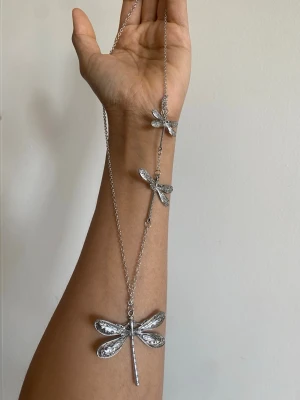 Silverfärgat halsband med trollsländor - Unikt halsband i silverfärg med tre detaljerade trollsländor i olika storlekar. Kedjan är tunn och smidig, och trollsländorna har fina mönster på vingarna som ger ett coolt och bohemiskt uttryck. Perfekt för dig som gillar naturinspirerade accessoarer.