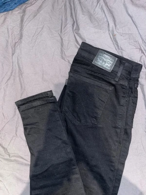 Svarta skinny jeans från Levis  - Svarta skinny jeans från Levis  med klassisk femficksdesign och hög midja. Jeansen har en stilren look med svarta sömmar och patch med logga bak i midjan. Perfekta för dig som gillar en tajt passform och enkel stil.