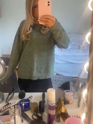 Grön stickad tröja med rund hals - Mysig stickad tröja i melerad grön färg med rund hals och ribbade muddar vid ärmslut och nederkant. Perfekt för lager-på-lager och passar till jeans eller kjol. Tröjan har en avslappnad passform och är tillverkad i ett mjukt material.