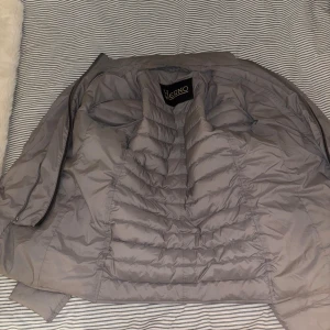 Grå dunblazer från Herno strl 48/medium - Säljer en snygg grå dunjacka från Herno med klassisk kavajkrage och knäppning framtill. Jackan är quiltad och har två fickor med knappdetaljer. Perfekt för dig som vill ha en stilren och lätt jacka med modern känsla.