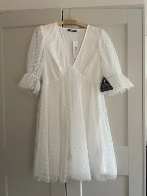 Vit prickig kortklänning Gina Tricot - Supersöt vit kortklänning från Gina Tricot med transparenta puffärmar och prickigt mönster. Klänningen har v-ringning, volangdetaljer vid ärmslut och är tillverkad i ett lätt, luftigt material som ger en romantisk känsla. Helt ny med alla lappar kvar!