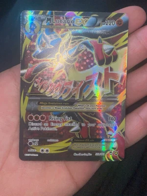Pokémonkort M Lucario EX Full Art 55 - Säljer ett Pokémonkort av typen M Lucario EX Full Art med holografisk yta. Kortet har färger i blått, rött, gult och svart och är tillverkat i laminerad papp. Kortet har 220 HP och attacken Rising Fist. Perfekt för samlare eller Pokémon TCG-spelare. Psa10 - 1000$