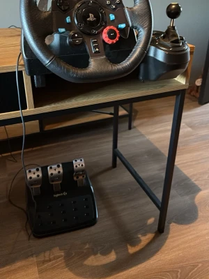 Logitech G29 ratt, pedaler & växelspak - Säljer ett Logitech G29 racing set med ratt, pedaler och växelspak. Ratten är svart med blå detaljer och PlayStation-knappar, pedalerna är i metall och plast, och växelspaken har en unik 8-ball växelknopp. Perfekt för racing på konsol eller PC.