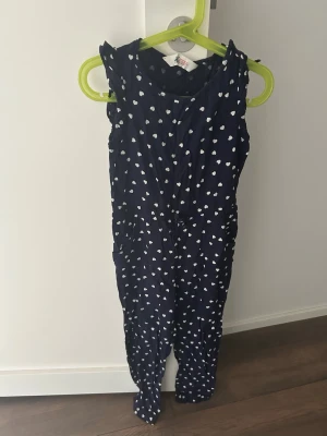 Mörkblå prickig jumpsuit H&M - Supersöt mörkblå jumpsuit från H&M med vita prickar. Ärmlös modell med rund hals och resår i midjan för skön passform. Perfekt för dig som gillar en lekfull och avslappnad stil. Tillverkad i mjukt och lätt material.
