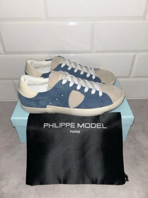 Philippe Model blåa sneakers mocka - Snygga sneakers Philippe Model i blå mocka med beige detaljer och vita skosnören. Klassisk låg modell med rund tå och vit sula. Perfekta för dig som gillar stilrena och trendiga skor med premiumkänsla.