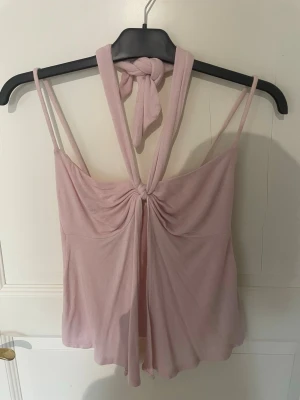 Ljusrosa linnetopp från Gina Tricot - Supersöt ljusrosa linnetopp från Gina Tricot med knyt i ryggen och tunna axelband. Toppen har en flowy passform och är perfekt för varma dagar. Materialet känns mjukt och lätt mot huden. Enkel men ändå stylish detalj med knuten i nacken.