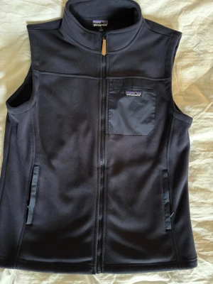 Mörkblå väst från Patagonia - Snygg mörkblå fleeceväst från Patagonia med dragkedja framtill och två fickor. Västen har en hög krage och en liten logotyp på bröstet. Perfekt för lager-på-lager och chill stil. Sorry för dålig bild min kamera är helt sönder, kontakta mig om ni vill ha bättre bilder kan eventuellt fråga en polare/föräldra om jag kan låna deras kamera. Priset är som alltid diskuterbart men tycker redan 699 är rimligt för denna.