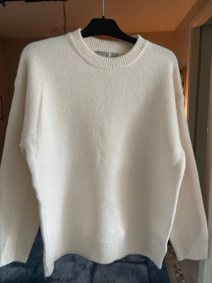 Vit stickad tröja rund hals - Klassisk vit stickad tröja med rund halsringning och långa ärmar. Tröjan har en enkel och stilren design utan synliga detaljer eller mönster. Perfekt för lager på lager och passar till det mesta. Materialet ser mjukt och bekvämt ut.