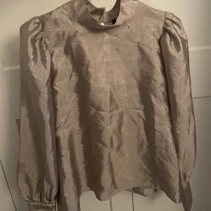  Blus fr Stockhlm med puff/ballongärm - Festlig och snygg beige/grå blus i glansigt material med ballongärmar och hög krage. Blus från MQ- Stockhlm i stl 38. Jag har vanligtvis 38 och tycker den känns lite stor på mig. 