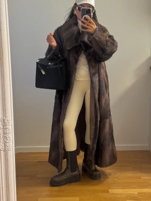 Mörkbrun lång Päls Kappa Pälskappa Pälsjacka Jacka Maxi - En elegant lång äkta Mink? Päls Kappa. Kappan har en bred krage och en rak oversized passform. Storlek passar fr S-M eller liten L.  Längd 122cm. Fr armhåla till armhåla 56cm. Ärmlängd fr axeln 63cm. Fint skick. Förutom ngt slitage på insidan.  Knäpps med 5hyskor