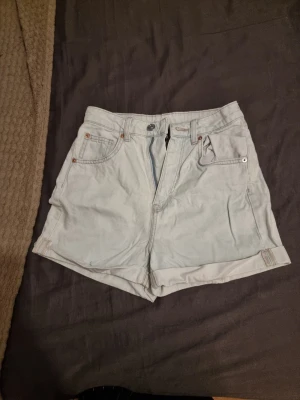 Ljusblå denimshorts från H&M - Säljer ett par ljusblå denimshorts från H&M i storlek 34. Klassisk femficksmodell med uppvikta benslut och knappgylf. Perfekta till sommaren och lätta att matcha med olika stilar.