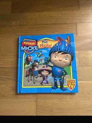 Riddare Micke & Varulven Valter böcker - Två färgglada barnböcker: 'Riddare Micke: Möt Micke!' med blå hård pärm och tecknade figurer från TV-serien, samt 'Varulven Valter: Ny i klassen' med mörkblå pärm och illustrerade barn och varulv. Perfekt för unga läsare som gillar äventyr och humor.