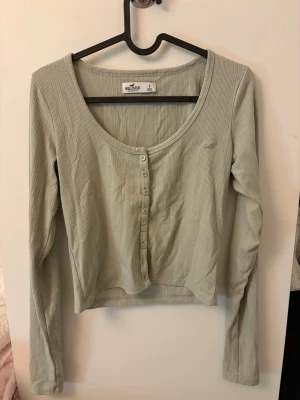 Ljusgrön ribbad kofta från Hollister - Superfin ljusgrön ribbad topp från Hollister med lång ärm och knappar framtill. Koftan är en äldre modell och har defekter (nopprig) därav priset. ❤️