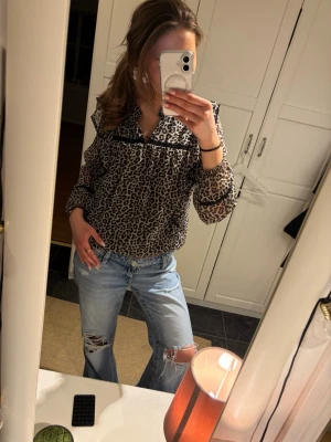 Leopardmönstrad blus med volang - Säljer en leopardmönstrad blus med volangdetaljer och svarta band. Blusen har långärmade transparenta ärmar och en rynkad krage. Materialet är tunt och lätt, perfekt för att skapa en cool look. Passar dig som gillar trendiga mönster och detaljer. Från Lindex barn i storlek 170! Passar perfekt till våren! Pris kan diskuteras vid snabb affär!💕