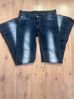 Cheap Monday utsvängda jeans blå - Säljer ett par blå utsvängda jeans från Cheap Monday med coola slitningar framtill. Jeansen har klassisk femficksmodell, normal midja och är tillverkade i denim med stretch. Perfekta för dig som gillar retrovibbar och vill sticka ut lite extra.