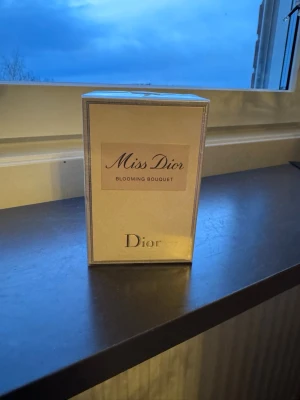 Miss Dior Blooming Bouquet parfym - Miss Dior Blooming Bouquet från Dior är en elegant parfym i en ljusbeige, rektangulär kartong med silverdetaljer. Förpackningen har en stilren design med märkets logotyp och doftnamnet tydligt på framsidan. Perfekt för dig som gillar lyxiga och fräscha dofter.