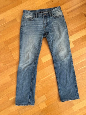 Blå raka jeans  - Ett par klassiska blå jeans med raka ben. Jeansen har fem fickor, normal midja och stängs med dragkedja och knapp. Perfekta för en avslappnad och trendig look.