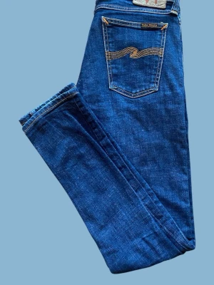 Nudie Jeans - Snygga blå jeans från Nudie Jeans med klassisk femficksdesign och kontrastsömmar på bakfickan. Jeansen har en rak passform och är tillverkade i denim av bomull. Perfekta för en avslappnad och trendig stil. 29/32 (Modellen Long John)