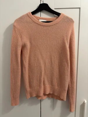 Persikofärgad stickad tröja - Mjuk och enkel persikofärgad stickad tröja med rund halsringning och långa ärmar. Tröjan har ribbstickade muddar vid ärmslut och nederkant, vilket ger en snygg och avslappnad look. Perfekt för att hålla sig varm under kyliga dagar. Nypris: 500kr därav lite högre pris. Går dock att diskutera pris😄 Bara använd 2 gånger, så den är som ny!