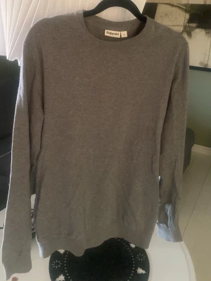 Grå stickad tröja från Kappahl - En enkel och stilren grå stickad tröja från Kappahl med rund halsringning och långa ärmar. Tröjan har ribbade muddar vid ärmslut och nederkant, perfekt för lager-på-lager. Passar dig som gillar en clean och klassisk look och perfekt nu på vår/sommar!
