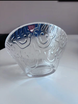 Orrefors skål med glada ansikten - Unik skål från Orrefors Sweden i transparent glas med reliefmönster av glada ansikten runt hela skålen. Skålen har en konisk form och är tillverkad i robust glas som ger en cool och lekfull känsla. Perfekt som dekoration eller serveringsskål.
