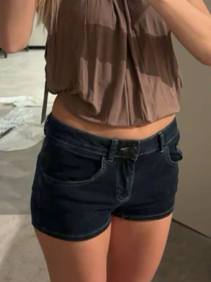 Mörkblå denimshorts med fickor - Snygga mörkblå jeansshorts med klassisk femficksdesign och låg midja. Perfekta för sommaren och lätta att matcha med olika toppar. Stängs med knapp och dragkedja framtill. Stolek 24