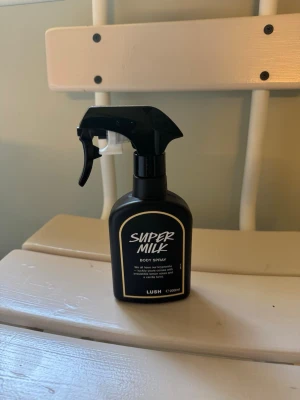 Lush Super Milk Body Spray parfym - Super Milk Body Spray från Lush i en svart plastflaska med spraymunstycke. Parfymen har en modern design och är enkel att använda tack vare sprayfunktionen. Flaskan rymmer 200 ml och har en stilren etikett med vit text.