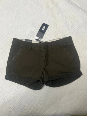 Mörkgröna shorts från Bik Bok - Snygga mörkgröna shorts från Bik Bok med hög midja och uppvikta benslut. Shortsen har två snedställda fickor fram och två fickor med lock och knapp bak. Perfekta för varma dagar och enkel att matcha med olika toppar.